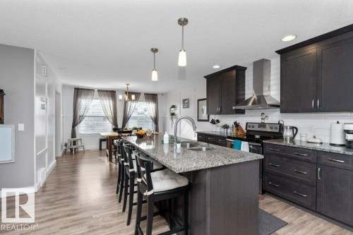 Kitchen with stainless steel electric range, dark stone countertops, a breakfast bar, light wood-style flooring, and an island with sink - 2607 20 Avenue, Edmonton, AB - Indoor Photo Showing Kitchen With Double Sink With Upgraded Kitchen