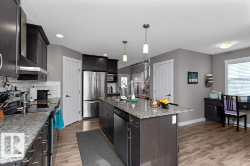 Kitchen with stainless steel appliances, light wood-style floors, light stone counters, hanging light fixtures, and a textured ceiling - 2607 20 Avenue, Edmonton, AB - Indoor Photo Showing Kitchen With Double Sink With Upgraded Kitchen