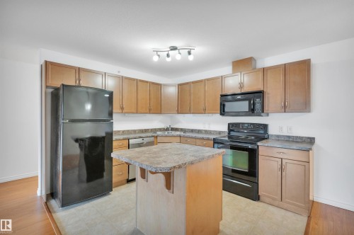 Kitchen with black appliances, a center island, a breakfast bar, wood finish cabinets, and light countertops - 422 7909 71 Street, Edmonton, AB - Indoor Photo Showing Kitchen