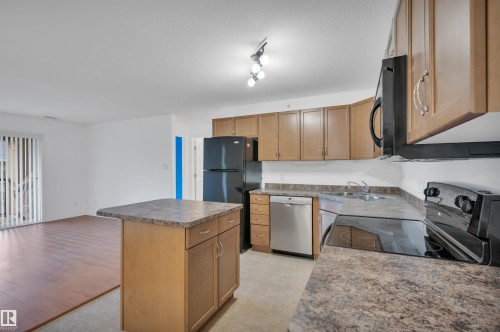 Kitchen featuring a kitchen island, black appliances, wood finish cabinetry, open floor plan, and dark countertops - 422 7909 71 Street, Edmonton, AB - Indoor Photo Showing Kitchen With Double Sink