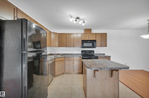 Kitchen featuring black appliances, dark countertops, a breakfast bar area, and wood finish cabinetry - 422 7909 71 Street, Edmonton, AB - Indoor Photo Showing Kitchen With Double Sink