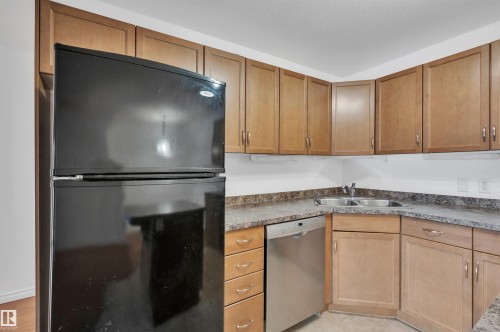 Kitchen featuring freestanding refrigerator, stainless steel dishwasher, wood finish cabinetry, and dark countertops - 422 7909 71 Street, Edmonton, AB - Indoor Photo Showing Kitchen With Double Sink