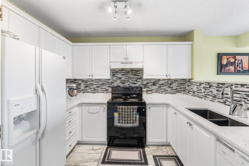 Kitchen featuring white appliances, white cabinets, light stone counters, light marble finish flooring, and a textured ceiling - 13148 151 Avenue, Edmonton, AB - Indoor Photo Showing Kitchen With Double Sink With Upgraded Kitchen