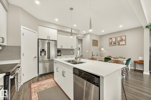 Kitchen with white cabinetry, pendant lighting, stainless steel appliances, a center island with sink, and backsplash - 74 Royal Street, St. Albert, AB - Indoor Photo Showing Kitchen With Stainless Steel Kitchen With Double Sink With Upgraded Kitchen