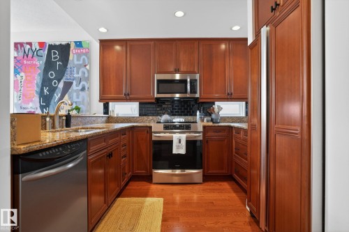 Kitchen featuring light stone countertops, stainless steel appliances, wood finish cabinetry, and recessed lighting - 1 9561 143 Street Nw, Edmonton, AB - Indoor Photo Showing Kitchen