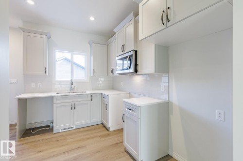 Kitchen featuring white cabinetry, stainless steel microwave, light wood-style flooring, decorative backsplash, and recessed lighting - 90 Dansereau Way N, Beaumont, AB - Indoor Photo Showing Kitchen