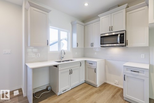Kitchen with stainless steel microwave, white cabinets, light wood-style flooring, decorative backsplash, and light stone counters - 90 Dansereau Way N, Beaumont, AB - Indoor Photo Showing Kitchen With Double Sink