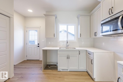 Kitchen featuring stainless steel microwave, light wood-style flooring, healthy amount of natural light, tasteful backsplash, and recessed lighting - 90 Dansereau Way N, Beaumont, AB - Indoor Photo Showing Kitchen