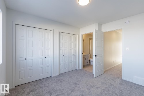 Unfurnished bedroom featuring two closets, light carpet, and connected bathroom - 90 Dansereau Way N, Beaumont, AB - Indoor