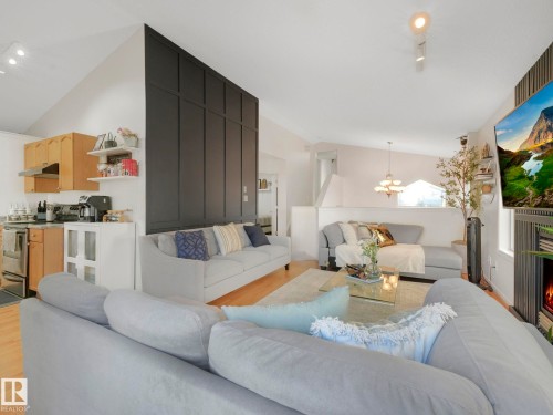 Living area with lofted ceiling, light wood-type flooring, suspended lighting, and a lit fireplace - 3239 21 Street, Edmonton, AB - Indoor Photo Showing Living Room