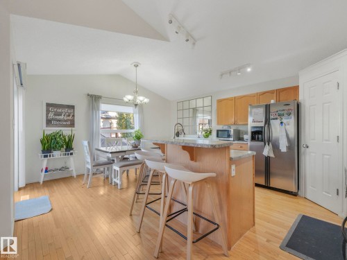 Kitchen with stainless steel appliances, a center island with sink, a breakfast bar, light wood-style flooring, and lofted ceiling - 3239 21 Street, Edmonton, AB - Indoor