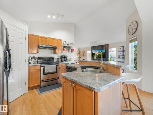 Kitchen with stainless steel appliances, light wood-style floors, vaulted ceiling, a center island with sink, and light countertops - 3239 21 Street, Edmonton, AB - Indoor Photo Showing Kitchen With Double Sink