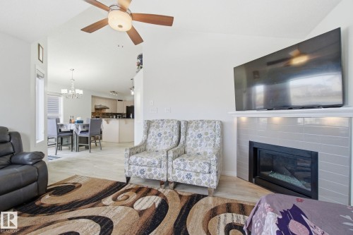 Living area featuring lofted ceiling, light wood-style floors, a glass covered fireplace, ceiling fan, and a chandelier - 3248 22 Street, Edmonton, AB - Indoor Photo Showing Living Room With Fireplace