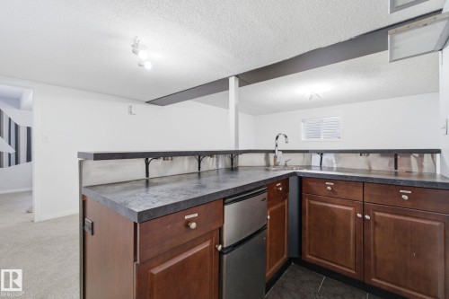 Kitchen with dark countertops, a textured ceiling, freestanding refrigerator, and a peninsula - 3248 22 Street, Edmonton, AB - Indoor Photo Showing Kitchen