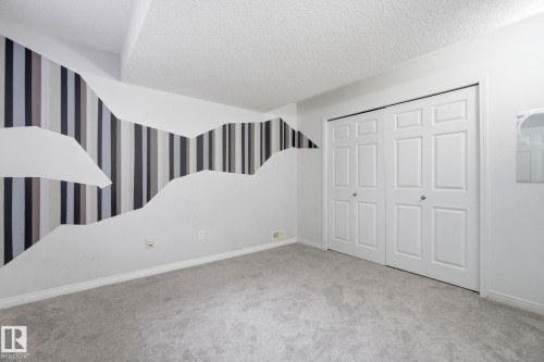 Unfurnished bedroom with wallpapered walls, carpet floors, a textured ceiling, and a closet - 3248 22 Street, Edmonton, AB - Indoor Photo Showing Bedroom