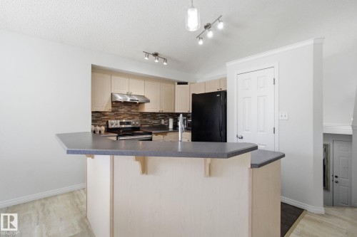 Kitchen featuring dark countertops, backsplash, freestanding refrigerator, and a kitchen bar - 3248 22 Street, Edmonton, AB - Indoor Photo Showing Kitchen