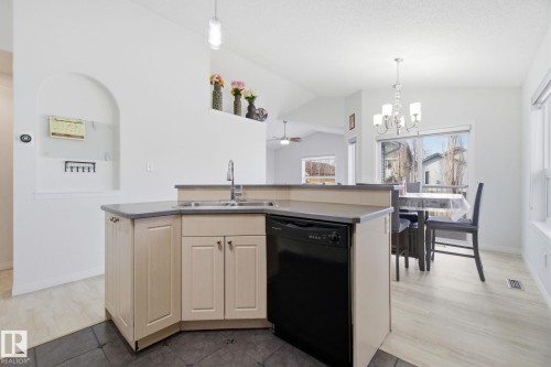 Kitchen with an island with sink, black dishwasher, vaulted ceiling, hanging lights, and light tile patterned flooring - 3248 22 Street, Edmonton, AB - Indoor Photo Showing Kitchen With Double Sink