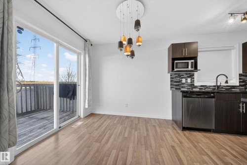 Kitchen featuring dark wood finish cabinetry, stainless steel appliances, light wood-style floors, a chandelier, and dark stone countertops - 5212 1A Avenue, Edmonton, AB - Indoor Photo Showing Kitchen With Double Sink