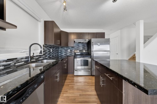 Kitchen with dark wood finish cabinets, stainless steel appliances, dark stone counters, light wood finished floors, and a textured ceiling - 5212 1A Avenue, Edmonton, AB - Indoor Photo Showing Kitchen With Double Sink With Upgraded Kitchen