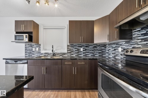 Kitchen featuring stainless steel appliances, range hood, dark stone countertops, light wood finished floors, and dark wood finish cabinets - 5212 1A Avenue, Edmonton, AB - Indoor Photo Showing Kitchen With Upgraded Kitchen