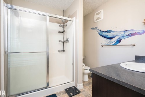 Bathroom featuring vanity, a stall shower, a textured ceiling, and light stone finish flooring - 13 5317 3 Avenue, Edmonton, AB - Indoor Photo Showing Bathroom