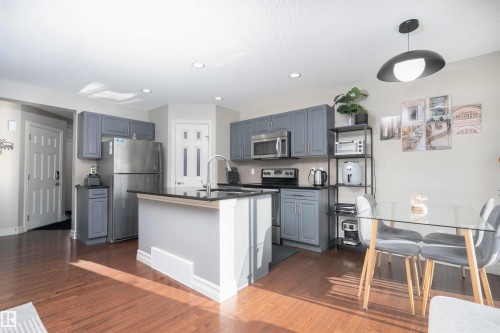 Kitchen with stainless steel appliances, a kitchen island with sink, dark wood-style floors, hanging light fixtures, and gray cabinets - 13 5317 3 Avenue, Edmonton, AB - Indoor Photo Showing Other Room