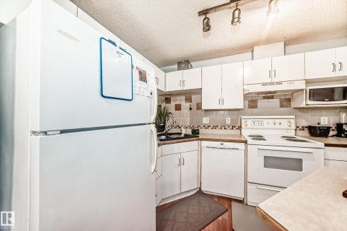 Kitchen with white cabinetry, white appliances, light countertops, a textured ceiling, and tasteful backsplash - 108 10535 122 Street, Edmonton, AB - Indoor Photo Showing Kitchen