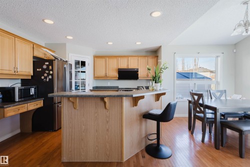 Kitchen with a breakfast bar area, dark countertops, freestanding refrigerator, dark wood-style floors, and a textured ceiling - 3534 Mclean Crescent, Edmonton, AB - Indoor