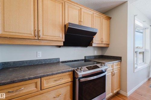 Kitchen with dark countertops, stainless steel electric range oven, exhaust hood, a textured ceiling, and light wood-type flooring - 3534 Mclean Crescent, Edmonton, AB - Indoor Photo Showing Kitchen
