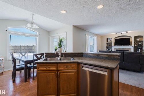 Kitchen with open floor plan, dishwasher, wood finish cabinetry, a textured ceiling, and hanging lights - 3534 Mclean Crescent, Edmonton, AB - Indoor Photo Showing Kitchen With Double Sink