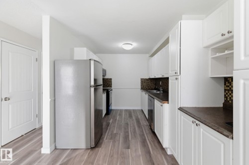 Kitchen featuring stainless steel appliances, tasteful backsplash, white cabinets, dark countertops, and light wood finished floors - 180 Londonderry Square, Edmonton, AB - Indoor Photo Showing Kitchen