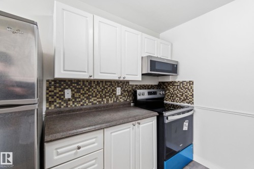 Kitchen with stainless steel appliances, white cabinets, tasteful backsplash, and dark countertops - 180 Londonderry Square, Edmonton, AB - Indoor Photo Showing Kitchen