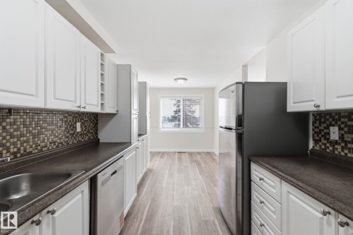 Kitchen with backsplash, white cabinets, dark countertops, stainless steel appliances, and light wood-style flooring - 180 Londonderry Square, Edmonton, AB - Indoor Photo Showing Kitchen