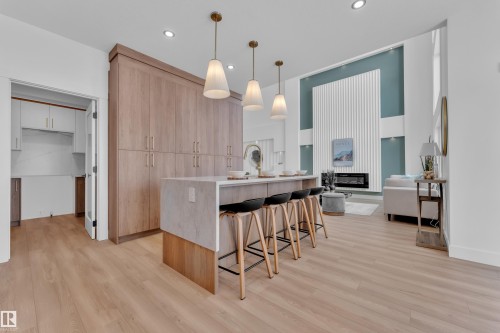 Kitchen with light wood finish cabinets, a breakfast bar, light wood finished floors, light stone counters, and decorative light fixtures - 228 Linden Loop, Leduc, AB - Indoor