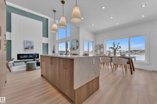 Kitchen with light wood-style floors, modern cabinets, light stone countertops, a glass covered fireplace, and decorative light fixtures - 228 Linden Loop, Leduc, AB - Indoor