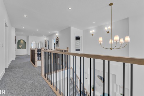 Corridor with light colored carpet, suspended lighting, and arched walkways - 228 Linden Loop, Leduc, AB - Indoor Photo Showing Other Room
