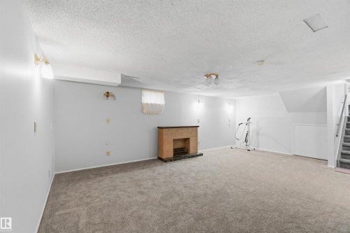 Basement with carpet flooring, a fireplace, and a textured ceiling - 135 Humberstone Road, Edmonton, AB - Indoor