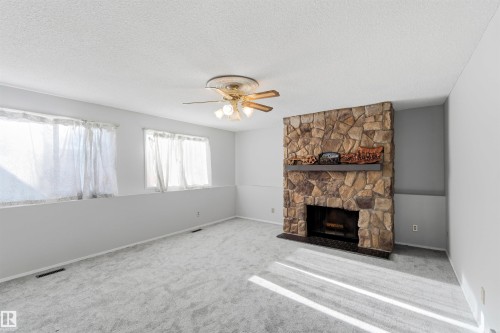 Unfurnished living room featuring carpet floors, ceiling fan, a fireplace, and a textured ceiling - 135 Humberstone Road, Edmonton, AB - Indoor Photo Showing Living Room With Fireplace
