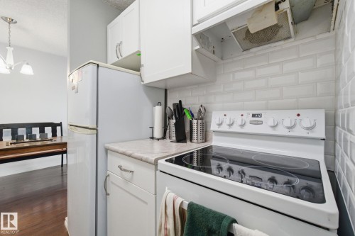Kitchen with white appliances, light countertops, white cabinets, exhaust hood, and a textured ceiling - 1312 13910 Stony Plain Road, Edmonton, AB - Indoor Photo Showing Laundry Room