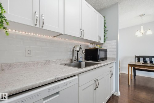 Kitchen with light countertops, dishwasher, white cabinets, backsplash, and dark wood-type flooring - 1312 13910 Stony Plain Road, Edmonton, AB - Indoor Photo Showing Kitchen