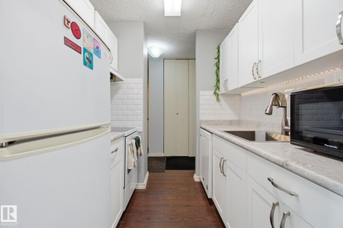Kitchen featuring white appliances, light countertops, white cabinetry, a textured ceiling, and dark wood finished floors - 1312 13910 Stony Plain Road, Edmonton, AB - Indoor Photo Showing Kitchen