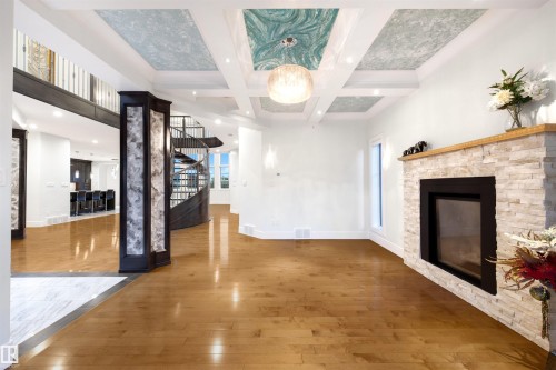Unfurnished living room with a stone fireplace, light wood-type flooring, coffered ceiling, recessed lighting, and ornamental molding - 4811 Woolsey Lane, Edmonton, AB - Indoor With Fireplace