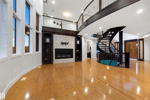 Unfurnished living room featuring a high ceiling, a stone fireplace, light wood-type flooring, and recessed lighting - 4811 Woolsey Lane, Edmonton, AB - Indoor Photo Showing Other Room With Fireplace