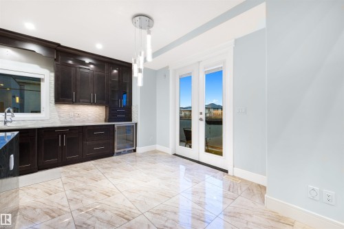 Kitchen with dark wood finish cabinetry, wine cooler, decorative light fixtures, decorative backsplash, and glass fronted cabinets - 4811 Woolsey Lane, Edmonton, AB - Indoor Photo Showing Kitchen