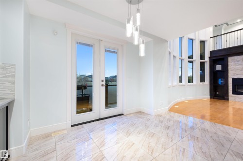 Unfurnished dining area featuring healthy amount of natural light, french doors, a stone fireplace, and light marble finish flooring - 4811 Woolsey Lane, Edmonton, AB - Indoor With Fireplace