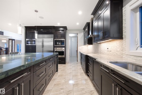 Kitchen with dark stone countertops, built in appliances, hanging light fixtures, light marble finish floors, and backsplash - 4811 Woolsey Lane, Edmonton, AB - Indoor Photo Showing Kitchen With Upgraded Kitchen