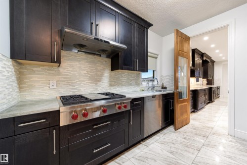 Kitchen featuring stainless steel appliances, light marble finish floors, light stone countertops, a textured ceiling, and tasteful backsplash - 4811 Woolsey Lane, Edmonton, AB - Indoor Photo Showing Kitchen With Upgraded Kitchen