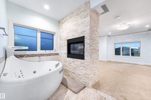 Bathroom with a tub with jets, light carpet, and a fireplace - 4811 Woolsey Lane, Edmonton, AB - Indoor Photo Showing Bathroom With Fireplace