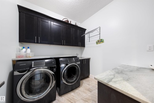 Laundry room with a textured ceiling, separate washer and dryer, and cabinet space - 4811 Woolsey Lane, Edmonton, AB - Indoor Photo Showing Laundry Room