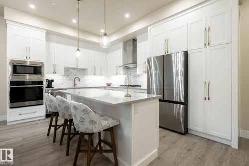 Kitchen featuring stainless steel appliances, pendant lighting, a kitchen bar, light wood-type flooring, and white cabinetry - 7471 May Common, Edmonton, AB - Indoor Photo Showing Kitchen With Upgraded Kitchen